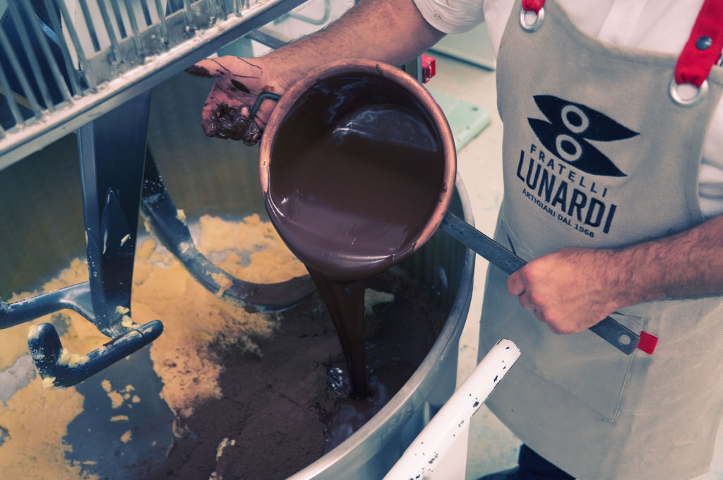 Hands draining melted chocolate from a copper pot